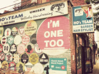 Digital colour photo of the side of Ho's Team Barber Hairstylist in Toronto, with all sorts of LGBTQ+ support painted directly on the bricks. A "Church Street Mural Project".