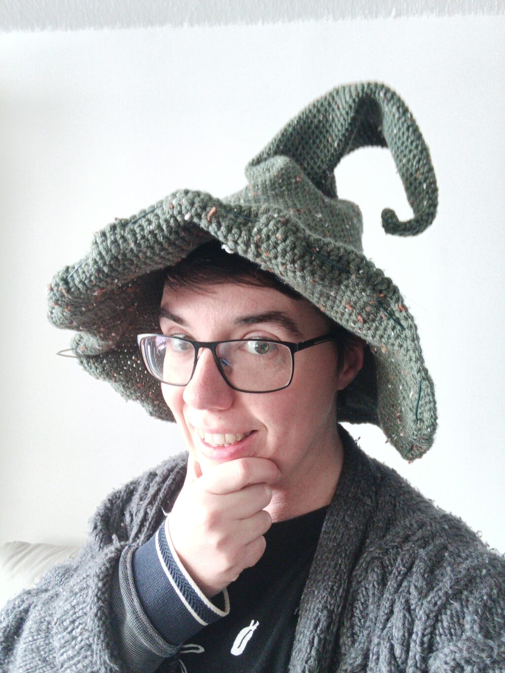 Photo of Jey wearing a green crocheted wizard hat and looking into the camera with a smile.